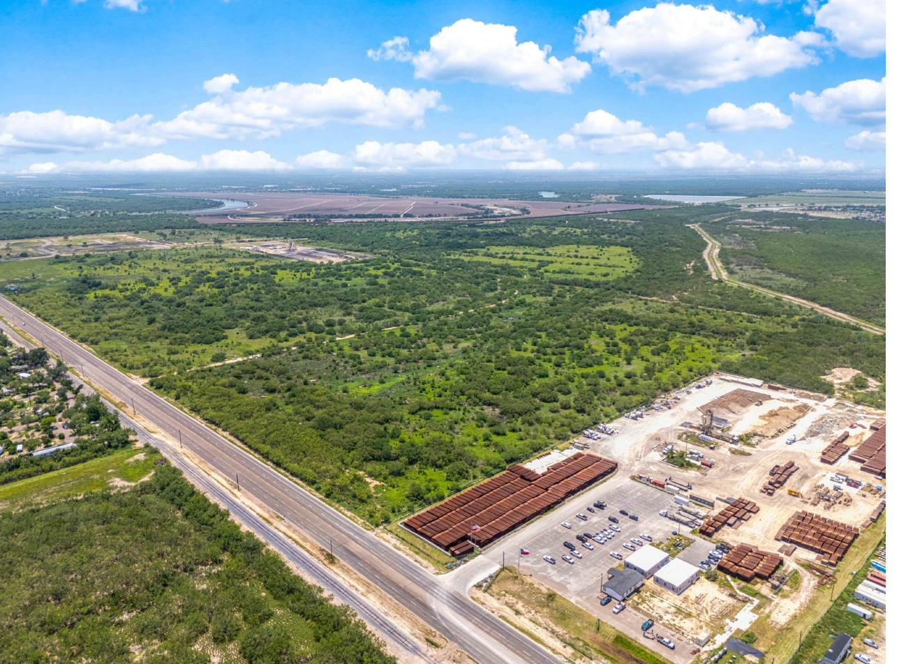 Wide aerial drone view looking south over the Mission Trade Center area showing the active industrial corridor along S. Conway Avenue, the railroad alignment, an operating steel pipe yard adjacent to the park, and the Rio Grande visible in the distance